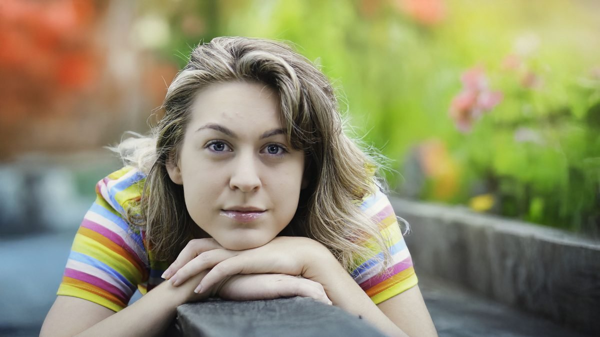 Outdoor portrait of a woman resting her chin on folded hands, soft garden colors behind her